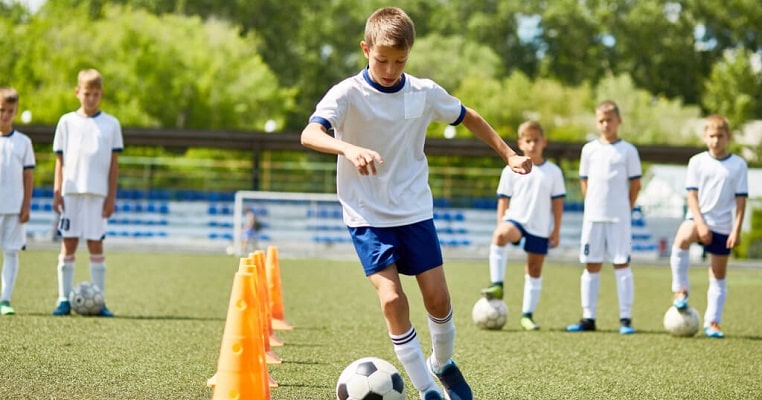 Foto de atletas em treinamento com bola e cone no campo de futebol